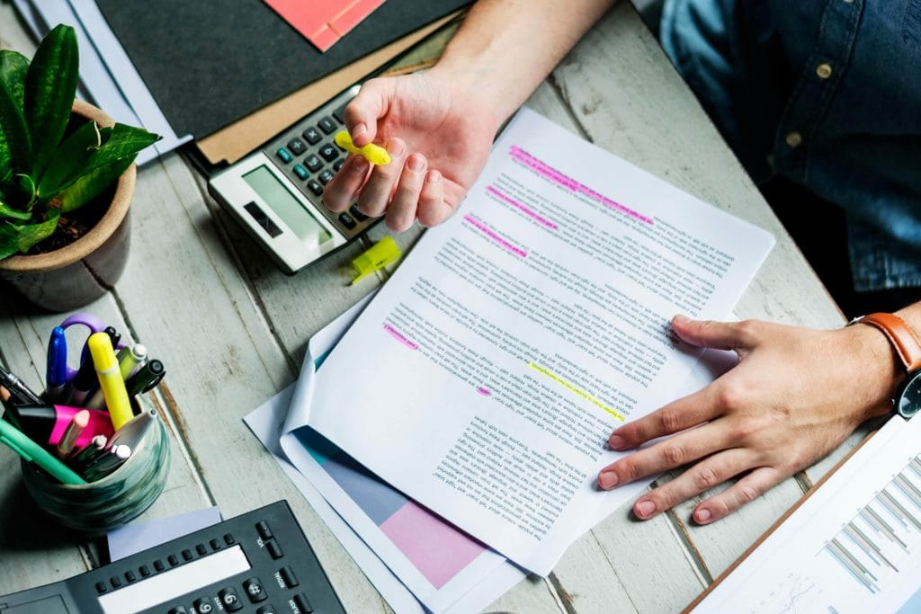 Person reviewing printed pages with highlighters and notes.