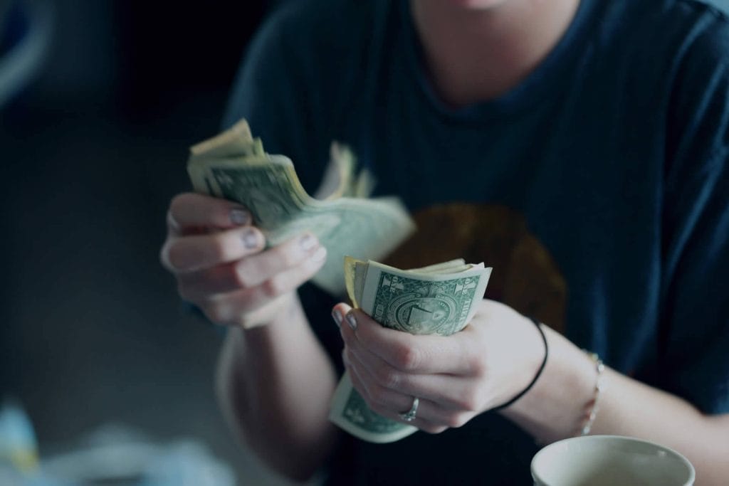 Person holding and counting cash at a desk with a calculator and coffee cup.