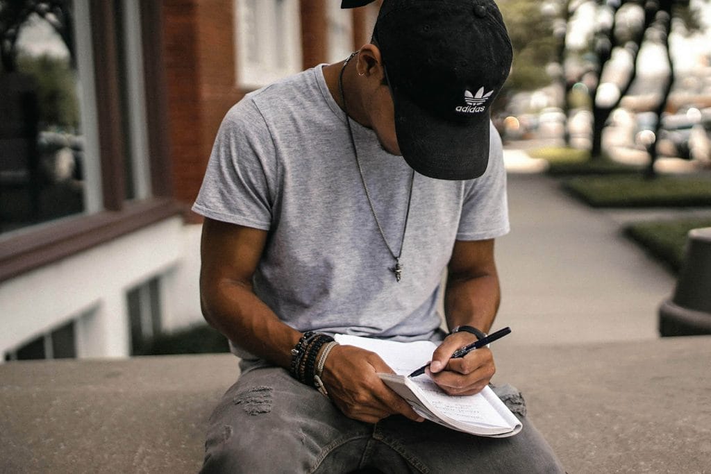 Person sitting outside and writing in a notebook, focused and thoughtful.