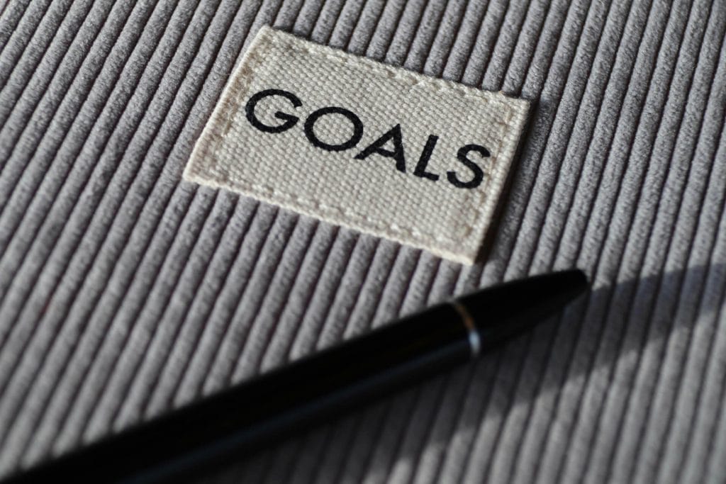 Black-and-white striped notebook labeled “Goals” with a pen beside it.